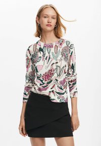 Pullover a maniche lunghe con stampa floreale in rosa, verde e nero su sfondo crema, abbinato a una gonna avvolgente nera.