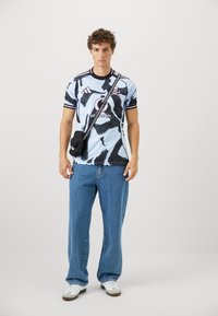 Tričko s krátkym rukávom v modro-čiernej vzorovanej kombinácii, s okrúhlym výstrihom, v kombinácii s voľnými modrými džínami a malou čiernou ramennou taškou.