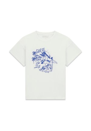 T-shirt blanc avec un motif bleu de palmiers, chaises longues, parasols, et le texte "GUESS Vivre ma meilleure vie sous le soleil."