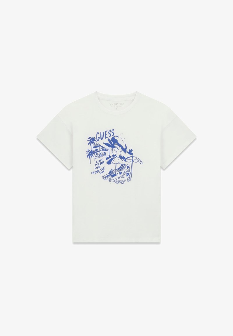 T-shirt blanc avec un motif bleu de palmiers, chaises longues, parasols, et le texte "GUESS Vivre ma meilleure vie sous le soleil."