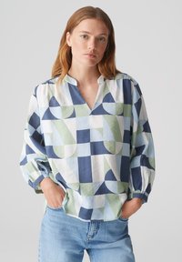 Blusa leggermente svasata realizzata in tessuto con motivi geometrici nei toni del blu navy, blu chiaro e verde, con scollatura a v e maniche gather.