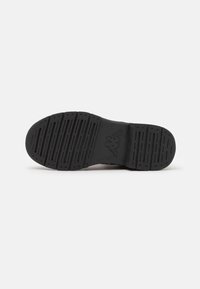 Semelle de chaussure de sport en caoutchouc noir avec un motif texturé ; comporte des rainures et des crêtes pour l'adhérence. Logo embossé près du talon.