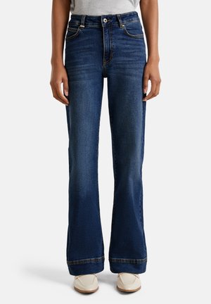 Dark blue flared jeans with a high waist, front pockets, and golden stitching. Features a textured denim fabric and visible seams.