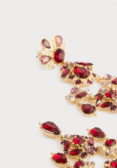 Gulltone øreringer med hengende mørkerøde og rosa edelstener akkompagnert av små hvite perler mot en lys bakgrunn.