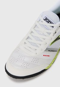 Scarpa da calcio sintetica bianca con pelle testurizzata, perforazioni sulla punta, suola nera e accento verde neon vicino alla suola. Logo in bianco e nero presente.