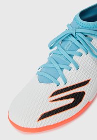 Baskets blanches avec une tige texturée, semelle orange, lacets bleu clair et un accent de logo noir sur le côté.