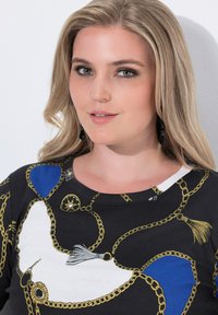 Svart topp med ett mönster av guldkedjor och fransar, blå accenter och rund halsringning. Slät tyg med en figurnära design.
