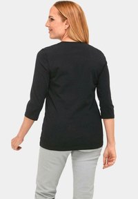 Zwarte top met driekwartmouwen van soft materiaal, met een ronde halslijn en een losse pasvorm, gecombineerd met lichtgrijze broek.