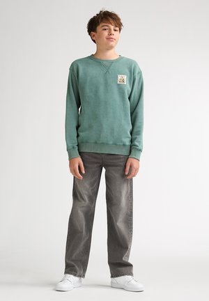 Groene katoenen trui met een ronde hals en een applicatie-embleem. Gecombineerd met grijze jeans met wijde pijpen en witte sneakers.