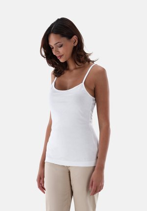 Weißes Tanktop mit dünnen Trägern, taillierter Passform, rundem Ausschnitt und weichem Material. Kombiniert mit beigen Hosen. Minimalistischer Stil.