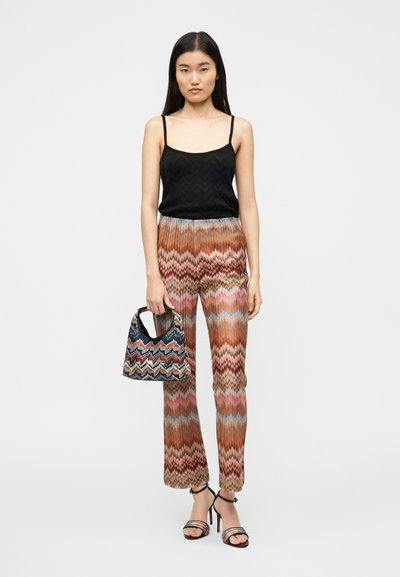 Haut noir texturé à bretelles spaghetti, motif en zigzag, pantalon fluide multicolore, sac à main noir à motifs colorés, sandales à talons.
