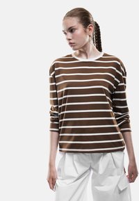 Bruin en wit gestreepte lange mouwen shirt met een ronde hals en een relaxte pasvorm, gecombineerd met losse witte broek. Gladde textuur en casual ontwerp.