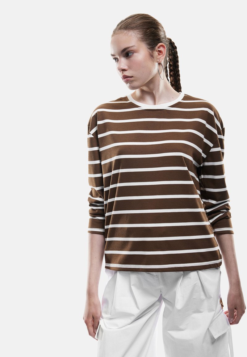 Bruin en wit gestreepte lange mouwen shirt met een ronde hals en een relaxte pasvorm, gecombineerd met losse witte broek. Gladde textuur en casual ontwerp.