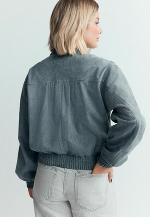 Szara bomberka zamszowa z prążkowymi mankietami i rantem, z plisą z tyłu dla swobody ruchów. Miękka faktura i casualowy design.