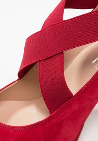 Chaussure compensée en suède rouge avec une large sangle élastique en croix. L'intérieur est doux, mettant en avant une doublure beige.