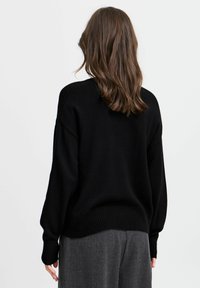 Schwarzer Strickpullover mit heruntergesetzten Schultern und geripptem Saum. Weiche Textur, lässige Passform und keine sichtbaren Muster oder Metallteile.