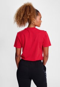Rød kortærmet bomulds t-shirt med rund hals, med sorte detaljer på skuldrene; parret med sorte bukser med elastisk talje.