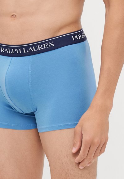 Mėlynos medvilninės bokserės su tamsiai mėlynu elastiniu juosmeniu, ant kurio balta spalva užrašyta "Polo Ralph Lauren". Lygus paviršius, prigludusi išvaizda.
