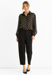 Black sheer blouse with gold leaf pattern, button-up design, long sleeves, paired with black trousers, slim-fit, tapered leg.