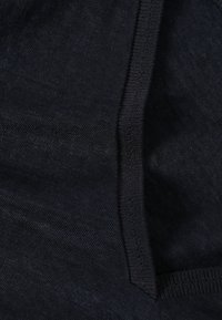 Gros plan sur un tissu foncé avec des coutures visibles et une texture tricotée, montrant une couture et un bord plié.