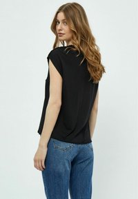 Zwart T-shirt met korte mouwen in een relaxed fit, zachte textuur en ronde halslijn, gecombineerd met blauwe denim jeans met klassieke zakken.