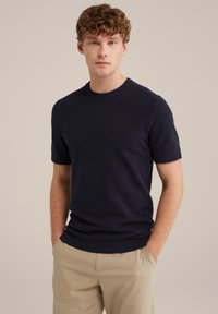Navy blue short-sleeve knitted sweater with a crew neck; features textured fabric and ribbed cuffs and hem; paired with light beige pants.