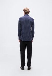 Μπλε σκούρο πουκάμισο με λευκές πουά, μακριά μανίκια και κλασικό γιακά. Μαύρο παντελόνι και παπούτσια ολοκληρώνουν το σύνολο.