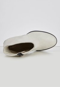 Stivaletto bianco alla caviglia con una superficie in pelle liscia, punta rotonda, zip laterale e una suola nera accentuata. Design minimalista senza motivi prominenti.