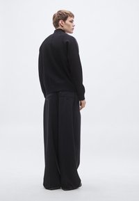 Zwarte trui met geribbelde manchetten en een hoge kraag, gecombineerd met ruime zwarte broeken met twee achterzakken en een losse pasvorm.