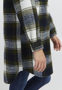 Plaid wool coat in dark green, navy, and white. Features a button cuff and a casual fit with side slits for ease of movement.