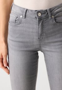 Grå, tettsittende jeans med midjehøyde, frontlommer og klassisk knappestengning. Glatt denimtekstur med subtile falmingdetaljer.
