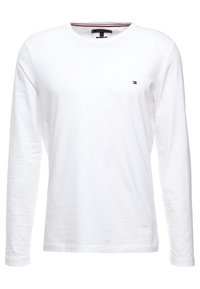 Bílé tričko s dlouhým rukávem a kulatým výstřihem, které má na hrudi malé barevné logo a strukturovanou tkaninu.