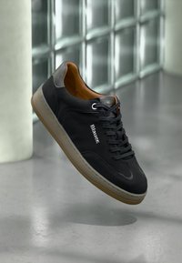 Schwarze Wildleder-Sneaker mit einer grauen Gummisohle und braunen Lederakzenten. Verfügt über eine runde Zehenpartie, Schnürung auf der Vorderseite und ein geprägtes Logo an der Seite.