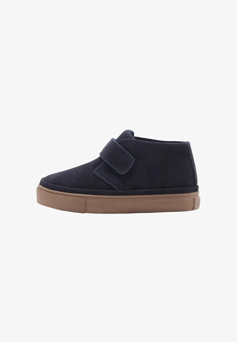 Chaussure chevillère en daim bleu marine avec une semelle en caoutchouc marron et une large fermeture à scratch, vue de profil sur un fond blanc.