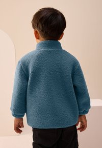 Pull-over en polaire bleu avec col montant, surface texturée et coupe décontractée. Caractérisé par des épaules tombantes et des poignets élastiqués.