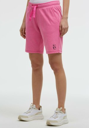 Person wearing pink drawstring shorts and white sneakers standing against a plain light background.