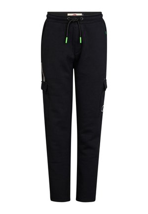Dreng stående iført en sort hættetrøje og sorte cargobukser med hvide sneakers mod en ensfarvet lys baggrund.