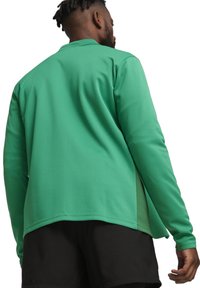 Groene sportjack met lange mouwen en een gladde textuur, met een relaxte pasvorm, zijsplitsingen en een contrasterende zwarte zoom, gecombineerd met zwarte shorts.