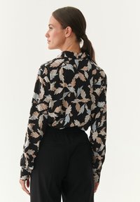 Long-sleeved black blouse featuring a multicolored leaf pattern in beige and light blue, with a collared neckline and relaxed fit.
