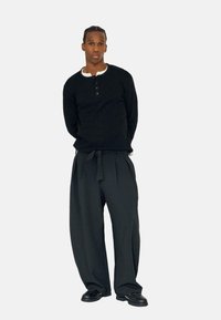 Sort langærmet sweater med knappedetaljer og hvid krave; løstsiddende sorte bukser med bindebælte; sorte sko. Enkel, klassisk design.