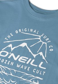 Camiseta de algodón azul con un diseño gráfico blanco que incluye texto e imágenes de montañas, con motivos de olas en la parte inferior.