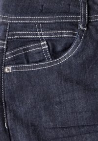Jeans de mezclilla azul oscuro con costuras blancas, un bolsillo delantero con un remache de metal y una textura suave.