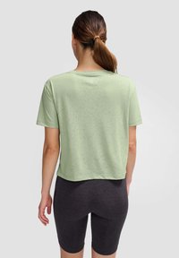 Jasnozielony, krótki T-shirt z krótkim rękawem, gładka textura i okrągły dekolt, w połączeniu z ciemnoszarymi szortami rowerowymi.