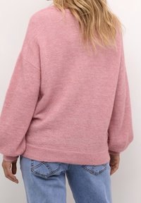 Hellrosa gestrickter Pullover mit lockerem Schnitt, weiten Ärmeln, geripptem Saum und glatter Textur, kombiniert mit hellblauen Jeans.