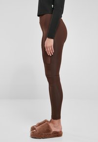 Legging marron taille haute en tissu extensible, doté d'une texture lisse et de coutures latérales. Associé à des chaussons marron pelucheux.