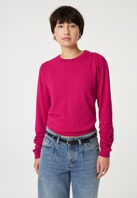 Getailleerde langemouwen top in felroze breiwerk, met geplooide details op de schouders en een ronde halslijn, gecombineerd met lichtblauwe high-waisted jeans.