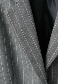 Grijze wollen blazer met een krijtstreepje patroon, voorzien van een reversed rever en een contrasterende zwarte voering. De stof heeft een gestructureerde afwerking.