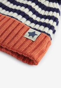 Bonnet tricoté avec des rayures bleu marine et blanches, muni d'un revers en orange côtelé. Comprend un patch avec une étoile bleue sur un fond de tissu clair.