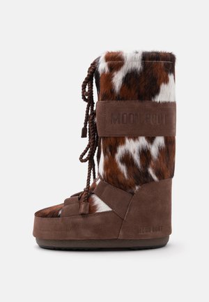 Wysokie zimowe buty w brązowo-białe futerkowe wzory z zamszowymi paskami i grubymi, plecionymi sznurowadłami, z logo "Moon Boot" na mankiecie i pięcie.