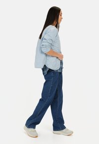 Lyseblå quiltet jakke med manchetter, lagd over en ternet skjorte, parret med løse blå denimjeans og lyse sneakers.